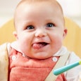 A baby smiling and playing with a spoon while having a meal
