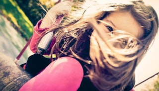 A tween girl on a swing with a hair covering her face