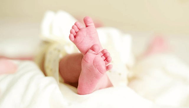 A newborn baby in white clothes lying down on a bed