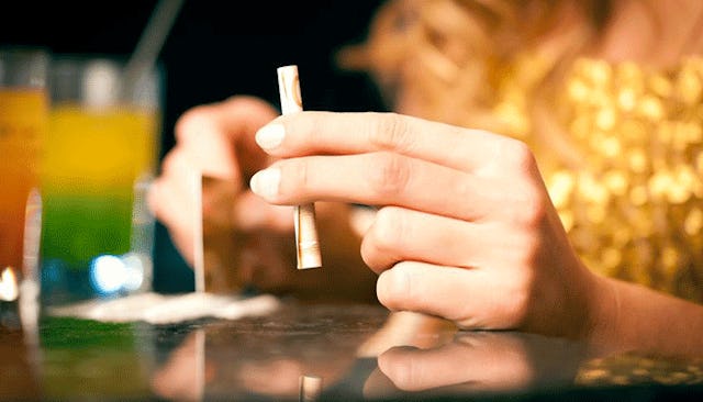 A woman holding money rolled into a tube-like shape on a table