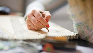 A woman's hand with red nail polish writing something down with a green pencil