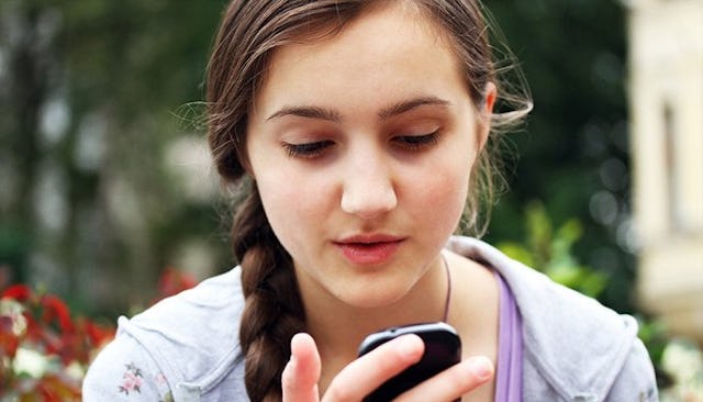 A teenage girl  holding a phone and looking at it