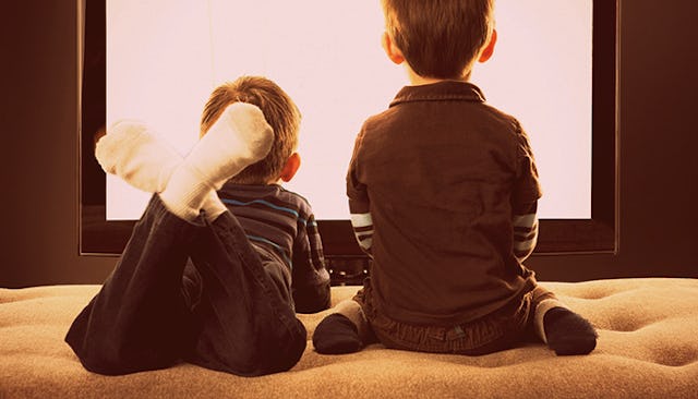 A boy sitting and a boy lying stomach down while watching TV