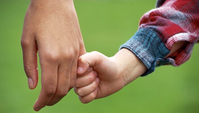 A kid holding his fathers hand.
