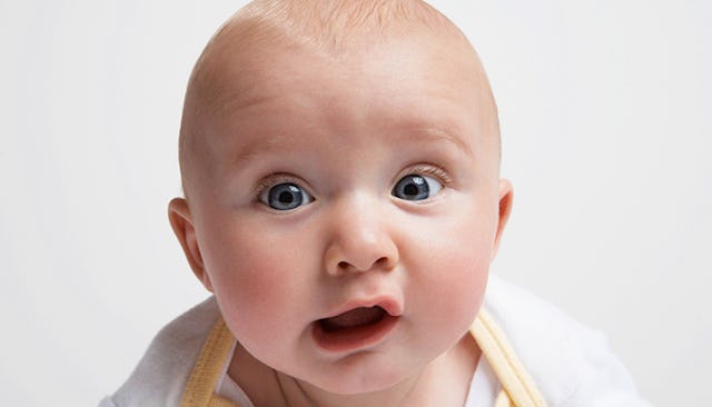 A baby with blue eyes and a goofy face looking confused