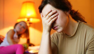 Desperate mom covering her face with her hand while her daughter is sitting in the background 