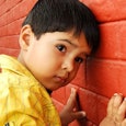 Sweet little boy leaning against an orange painted wall, dealing with his autism.