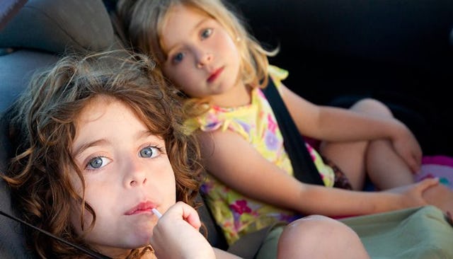 Two small girls sitting together in the backseat of a car on their way to a playdate 