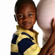 A boy holding his pregnant mothers stomach and putting his ear to it.
