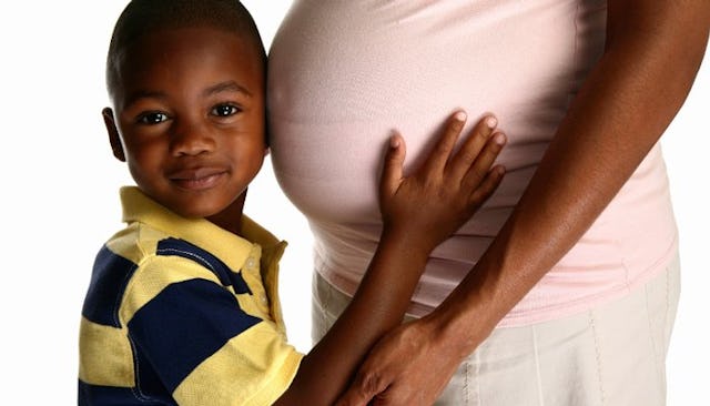 A boy holding his pregnant mothers belly and placing his ear to it.