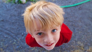 A blonde boy with blue eyes who is a wild child smiling and looking up