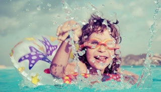 A little girl wearing swimming goggles while having fun in the water.