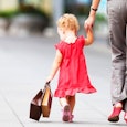 A mother walking the street with her daughter wearing a red dress, both carrying shopping bags