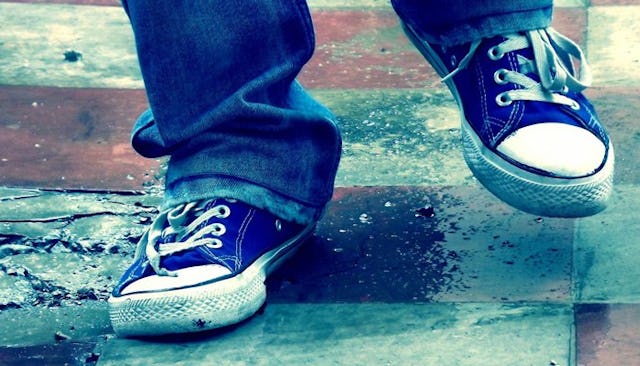 A small girl wearing jeans that drape over her worn out blue converse