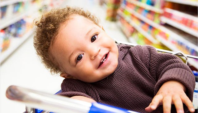 A smiling baby in the shopping cart in the supermarket store