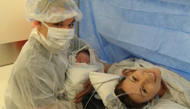 A father holding his newborn baby next to the smiling mom in a hospital bed immediately after a C-se...