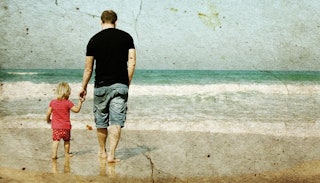 A young father wearing a black t-shirt is holding his son's hand while walking toward the sea during...