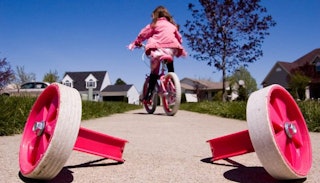 A young girl riding her pink bicycle, leaving the training wheels behind.