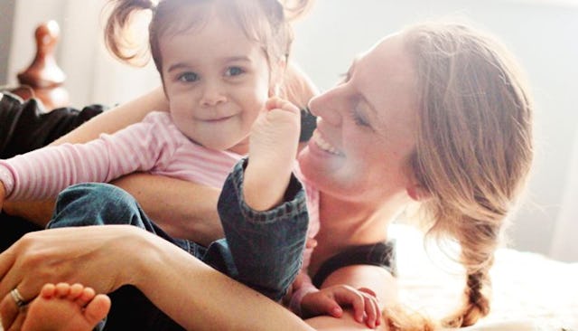 A mother playing and having fun on the bed with her second daughter