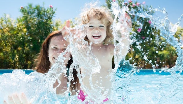 A mother playing with her daughter in the pool, while daughter is splashing the water