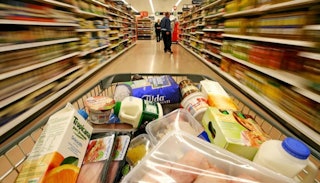 A shopping cart filled with groceries surrounded by two blurred isles on the side in a grocery store