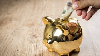 Someone putting a 100 dollar bill into a golden piggy bank