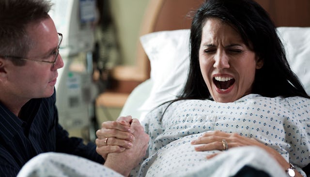 A woman experiencing childbirth pain in a hospital bed with her husband holding her hand