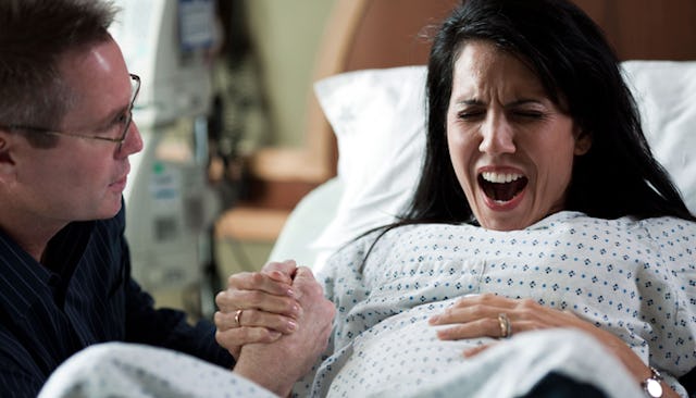 A woman experiencing childbirth pain in a hospital bed with her husband holding her hand 