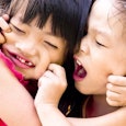 Two small girls playing together and pinching each other's cheeks. 