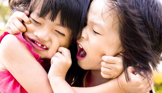 Two small girls playing together and pinching each other's cheeks.