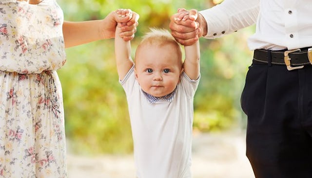 Parents holding their young boy by hands in a park while he is wearing a blue T-shirt