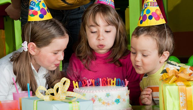 Two girls and a boy blowing candles out candles on a cake at a birthday party