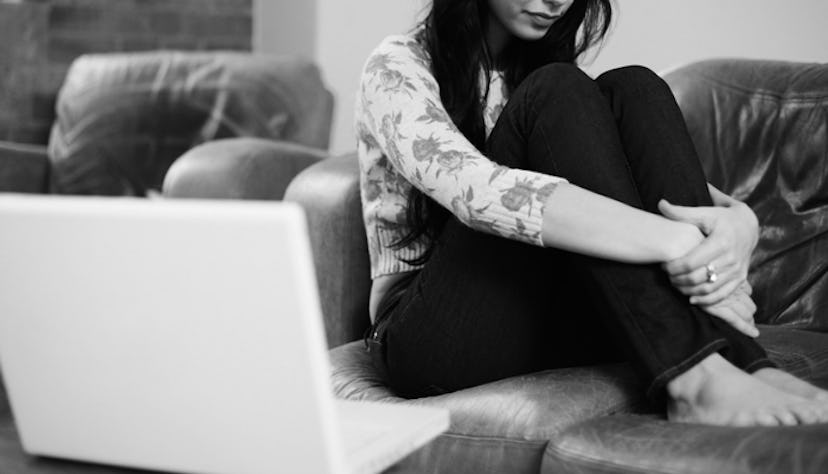 A woman with depression sitting curled up on a couch with a laptop open next to her