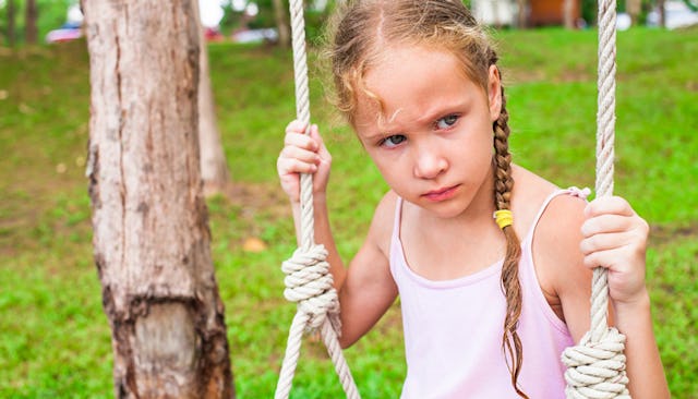 A grieving in a pink tip on sitting on a swing with a sad facial expression