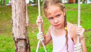 A grieving in a pink tip on sitting on a swing with a sad facial expression