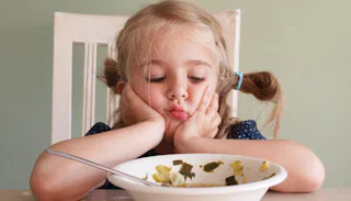 A girl sitting at thediningg table looking sadly at her plate