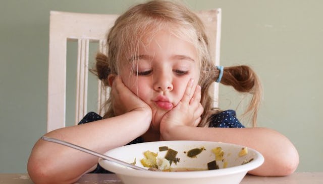 A girl sitting at the dining table looking sadly at her plate.