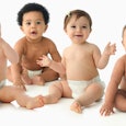 Four babies in diapers, sitting and smiling.