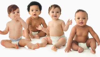 Four babies in diapers, sitting and smiling.