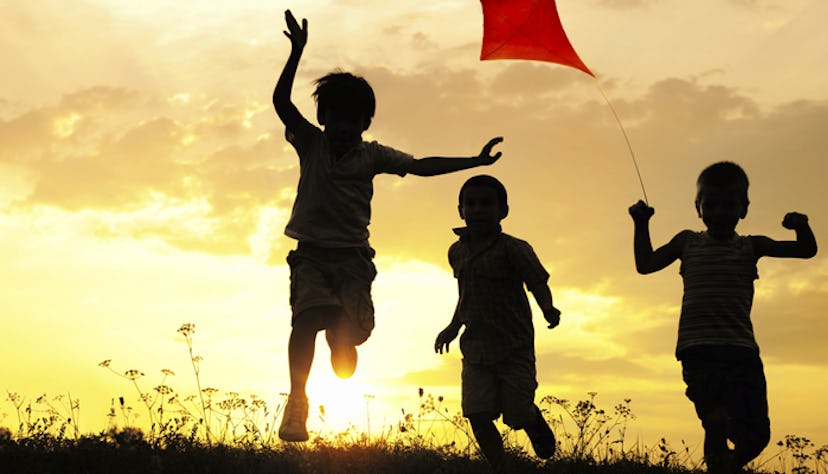 Three boys running with a kite during the sunset