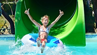 A child on a floatie going down a slide at a water park being happy