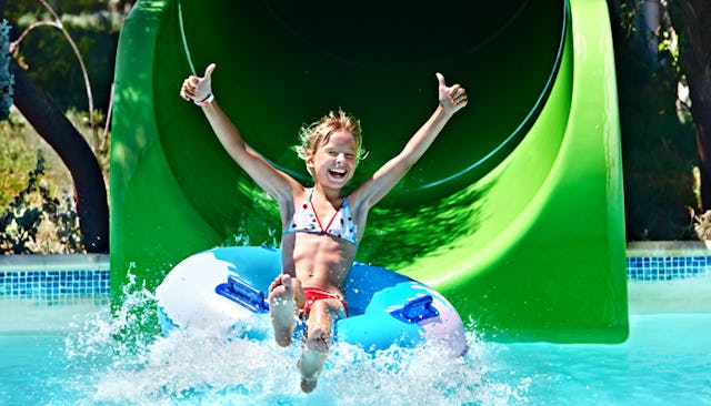 A child on a floatie going down a slide at a water park being happy