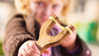 A kid holding a sling and pointing it at the camera.