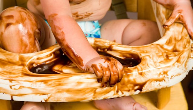 A baby sitting on a baby chair and making a mess with chocolate