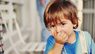 A strong-willed child in a blue shirt with his hand over his mouth