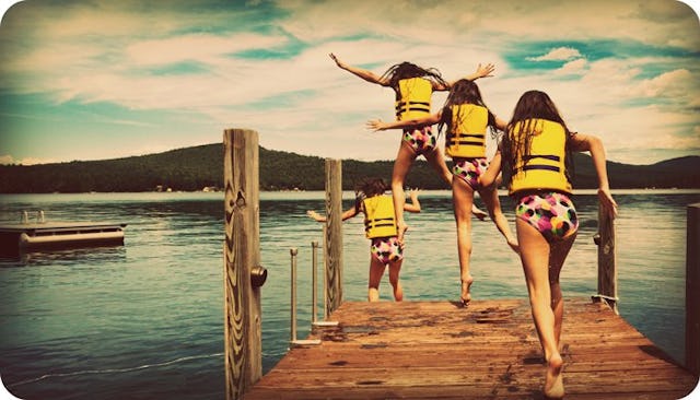 Four girls jumping into the lake at an overnight camp with life vests on 