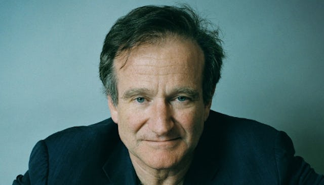 A portrait of Robin Williams wearing a black shirt with a neutral facial expression, and a light tea...