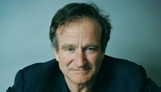 Robin Williams wearing a black shirt looking serious, and a light teal blue wall behind him