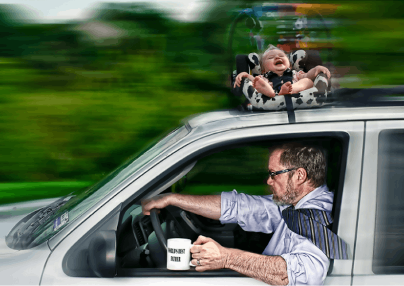 Father holding a cup and driving his car fast with a kid in a baby car seat on top of the car laughi...