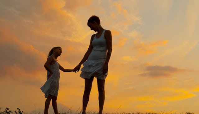 A mother and daughter standing and holding hands with a sunset in the background